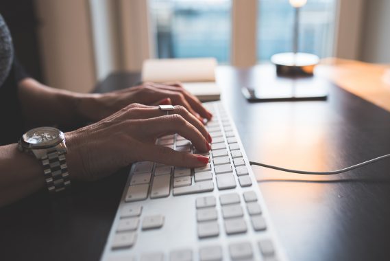 Woman typing on keyboard on desk, tapping keys to send a message on computer