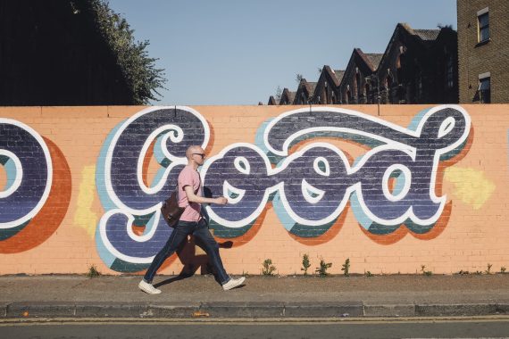 Walking in front of a brick wall that says 'good' in a mural - suggesting walking is good for you