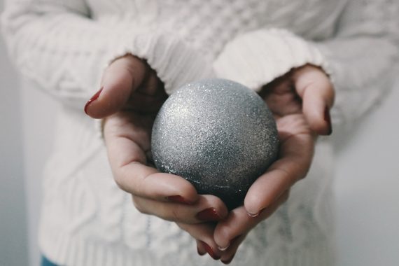 Silver bauble in hands of woman wearing winter jumper, representing Christmas and sensory stimulation - a worry for children with Autism