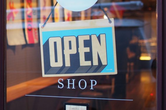 Shop open sign on retail outlet with goods in background to illustrate sales tactics by retailers including on Black Friday