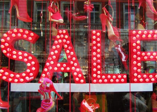 Sale sign in big red letters with lighting, surrounded by red shoes in a range of styles