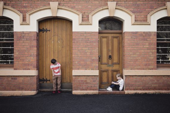 Children in doorways: one standing in front of ornate wooden door, the other sitting in front of smaller door, showing child poverty comparisons