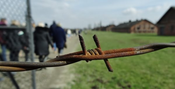 Group understanding trauma and suffering at Auschwitz-Birkenau concentration camp to remember the Holocaust and educate themselves with a group tour of the area, seen through barbed wire.