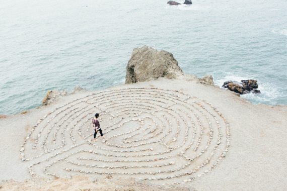 Walking through maze or labyrinth of decisions by rocks and sea.