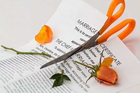 Marriage contract cut up with orange scissors and broken flower laid on top, symbolising separation and divorce