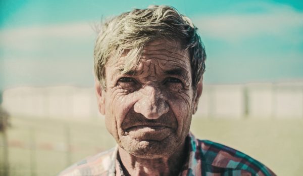 Elderly man with deep-set wrinkles faces camera with outdoor background out of focus