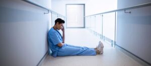Medic in hospital corridor sat on floor with hand against head