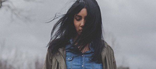Woman alone and upset against grey sky, symbolising learned helplessness and inaction