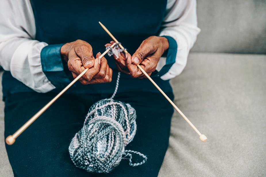 Woman knitting in blue and white jacket with needles and wool to demonstrate a craft hobby with Alzheimer's
