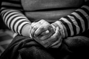Elderly lady in black and white image of clasped hands demonstrating care for older people and carers