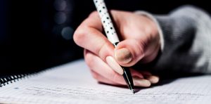 Student writing university essay by hand on paper, with peach nail varnish and spotty pen