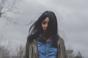 Lone woman looking down surrounded by stormy clouds and grey skies suggesting torment or upset