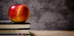 School desk and books and apple with blackboard in the background